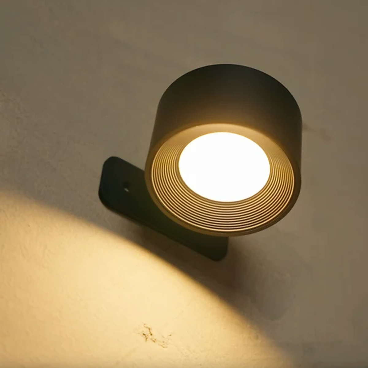Close-up of the black wall sconce with warm LED glow on a textured wall